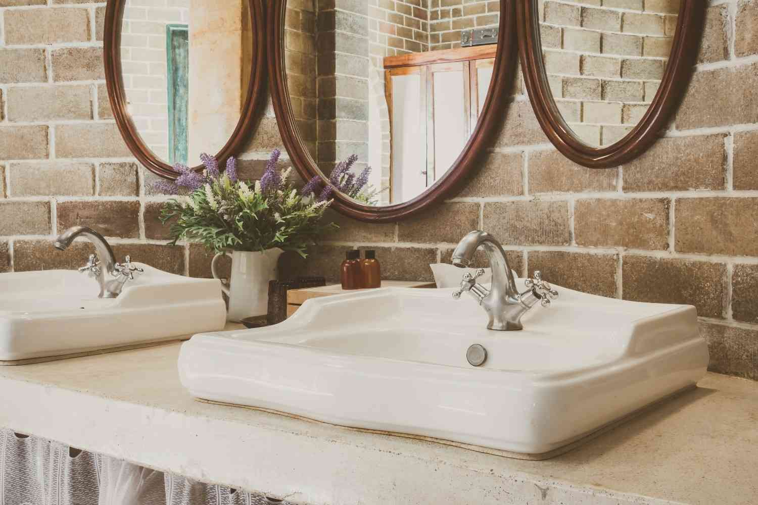 Vintage-style double sink vanity with oval mirrors and a brick wall