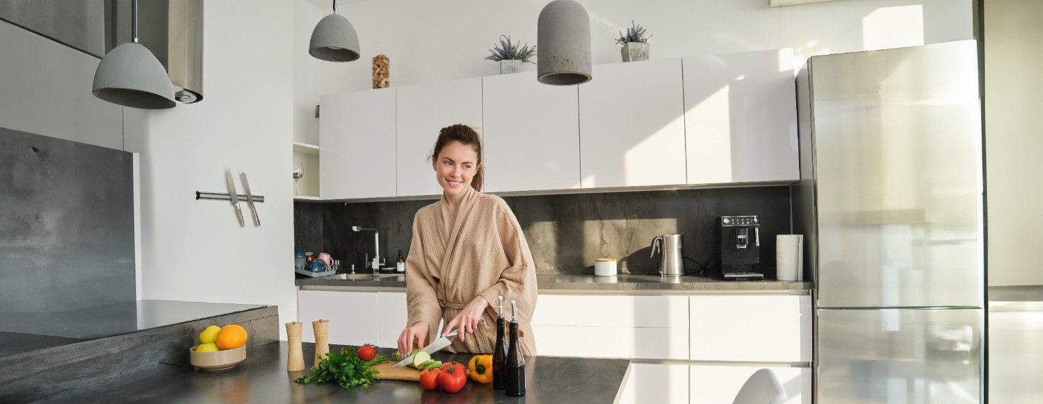 Smiling woman preparing vegetables in a bright modern kitchen with white cabinets