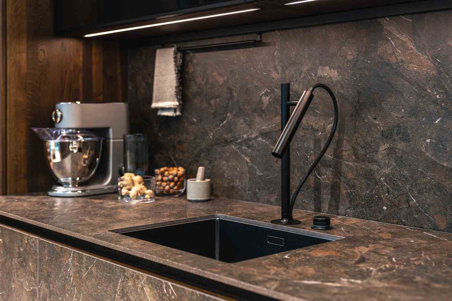 Dark stone countertop and backsplash with a black undermount sink and faucet