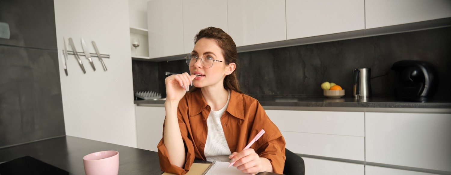 Woman in a modern kitchen thinking and taking notes while planning a remodel
