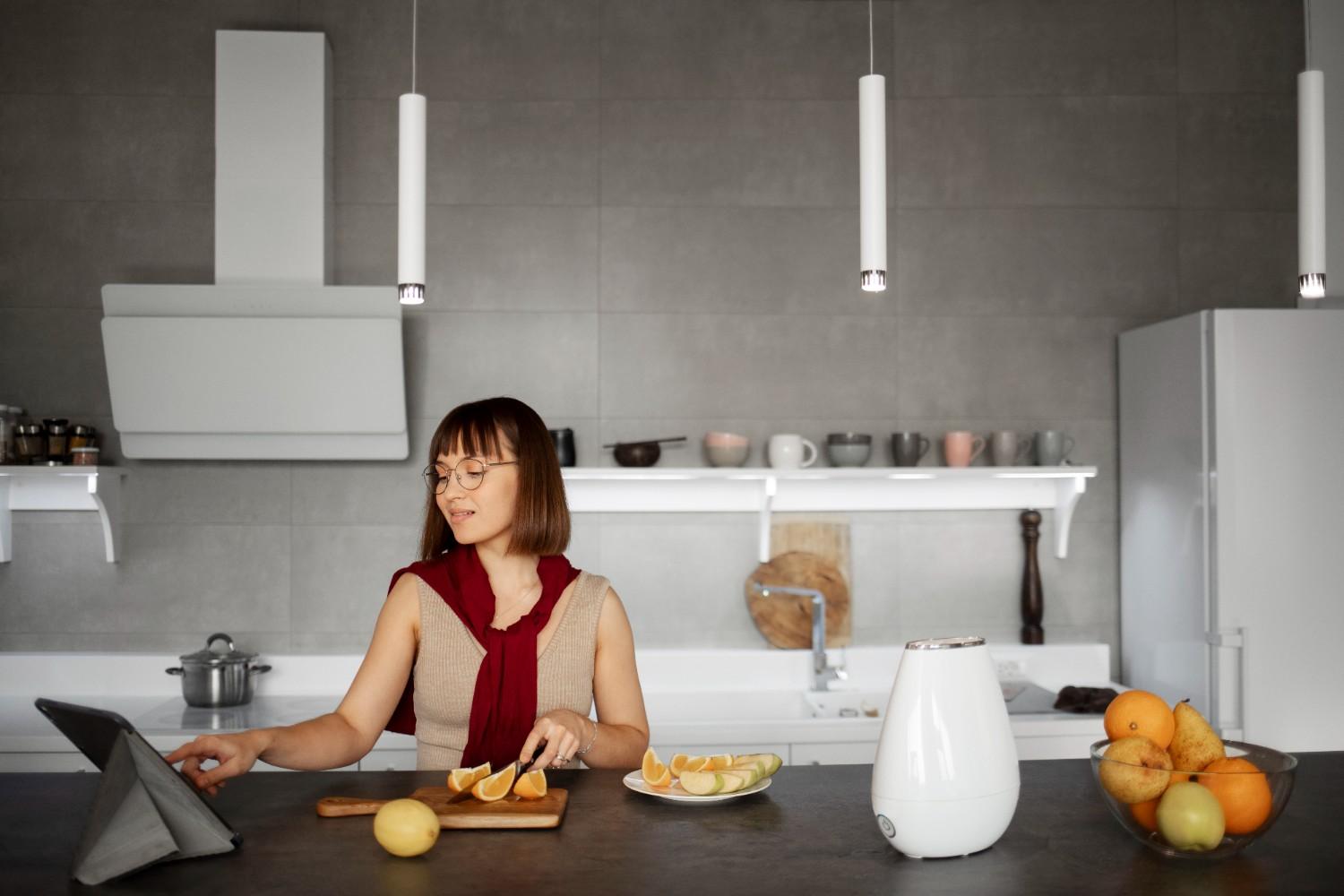 Woman slicing fruit at a modern kitchen island while using a tablet